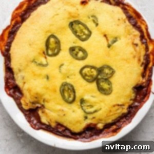 Hearty Chili Pot Pie 10 A baked dish in a round white pan, topped with cornbread and sliced jalapenos, with some edges browned and crispy.
