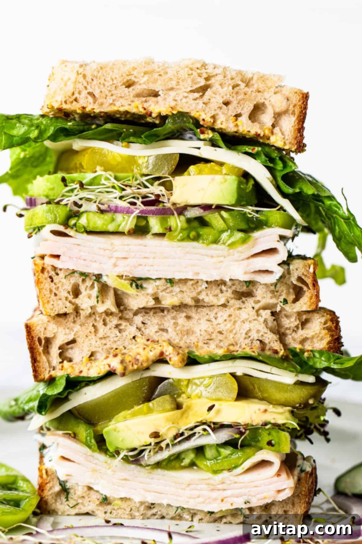 A perfectly stacked, tall turkey sandwich on a ceramic plate, showcasing multiple layers of fresh ingredients and premium deli turkey.