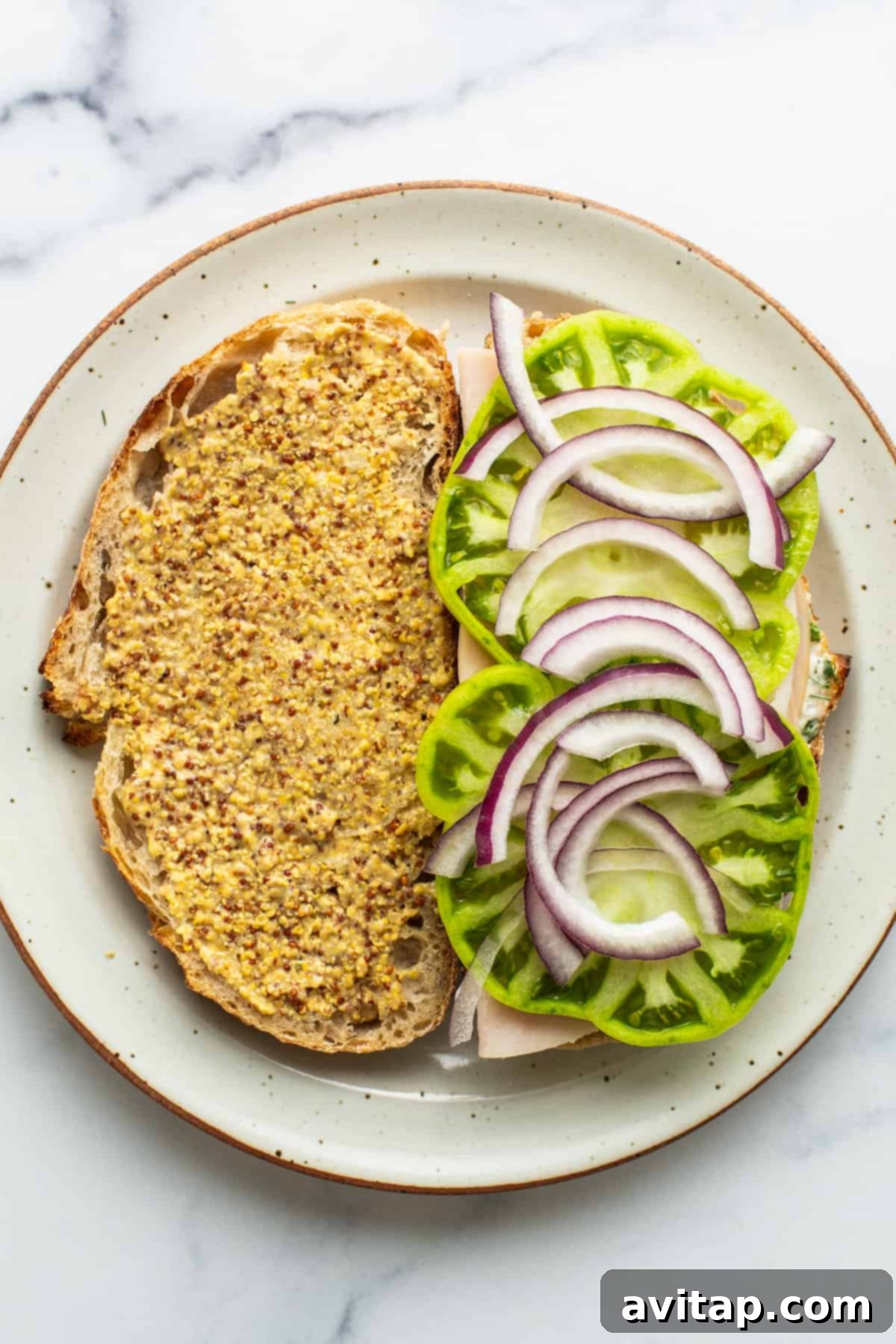 An open-faced turkey sandwich showing layers of crisp lettuce, refreshing cucumber slices, and thinly sliced red onion on sourdough bread.