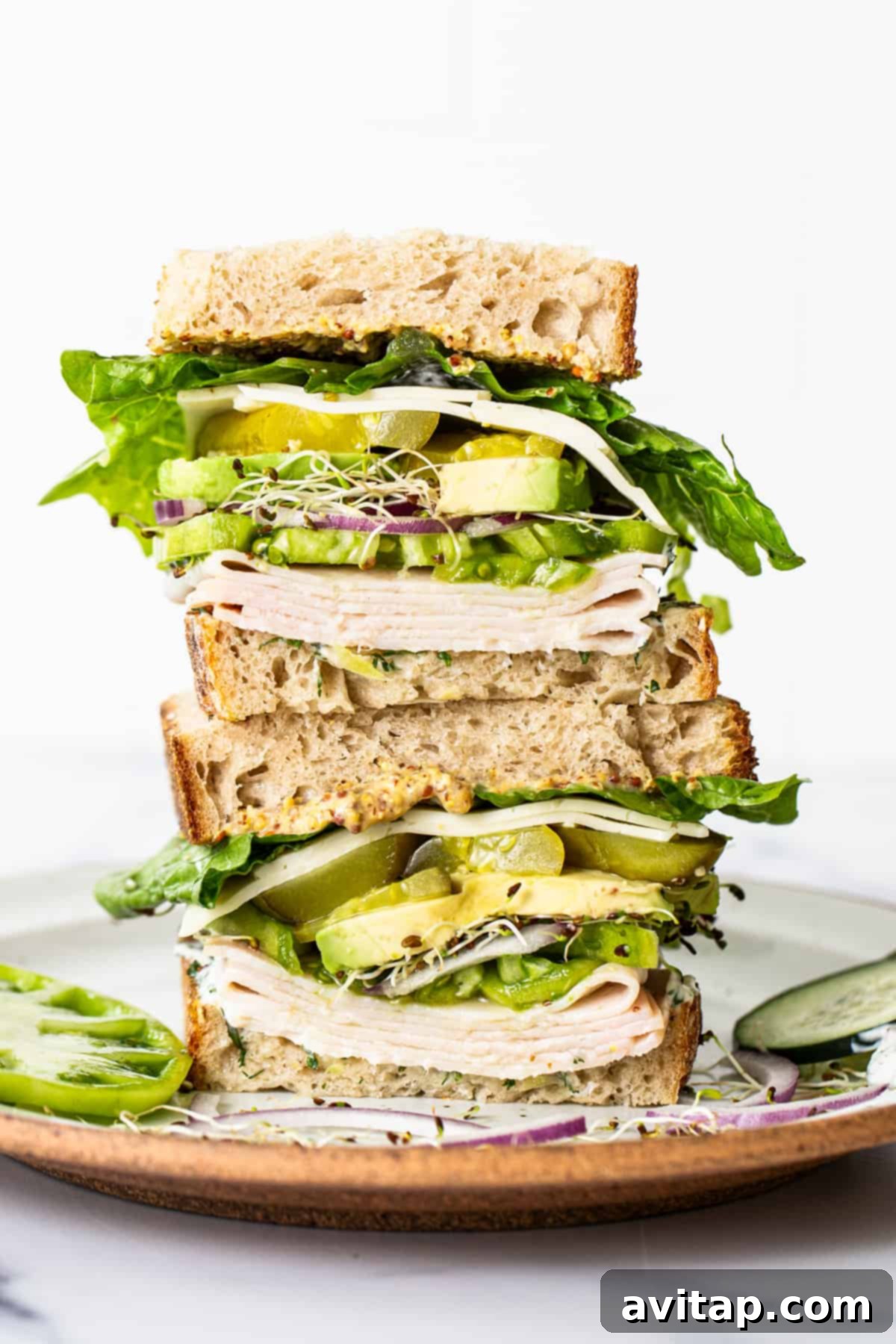 A beautifully assembled tall turkey sandwich on a ceramic plate, showcasing all the fresh layers and rich fillings.