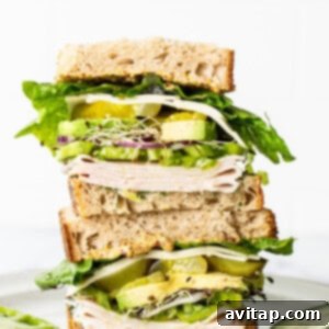 A close-up of a perfectly constructed turkey sandwich, with visible layers of turkey, cheese, and fresh vegetables on hearty bread.