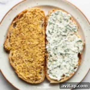 Two slices of bread on a plate, one topped with mustard and herbs, the other with a creamy white spread and chopped dill.
