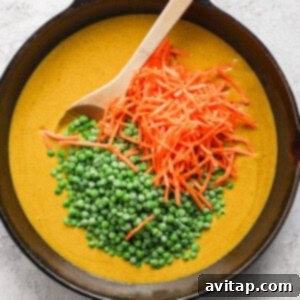 A cast iron skillet containing creamy soup garnished with a spoonful of green peas and a scattering of grated carrots on a light-colored surface.