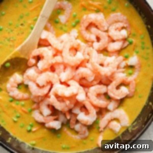 A skillet filled with a creamy pea soup topped with a mound of cooked shrimp, with a wooden spoon resting inside the pan.