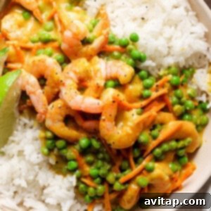 A bowl of white rice topped with shrimp and green peas in a creamy sauce, garnished with a lime wedge.