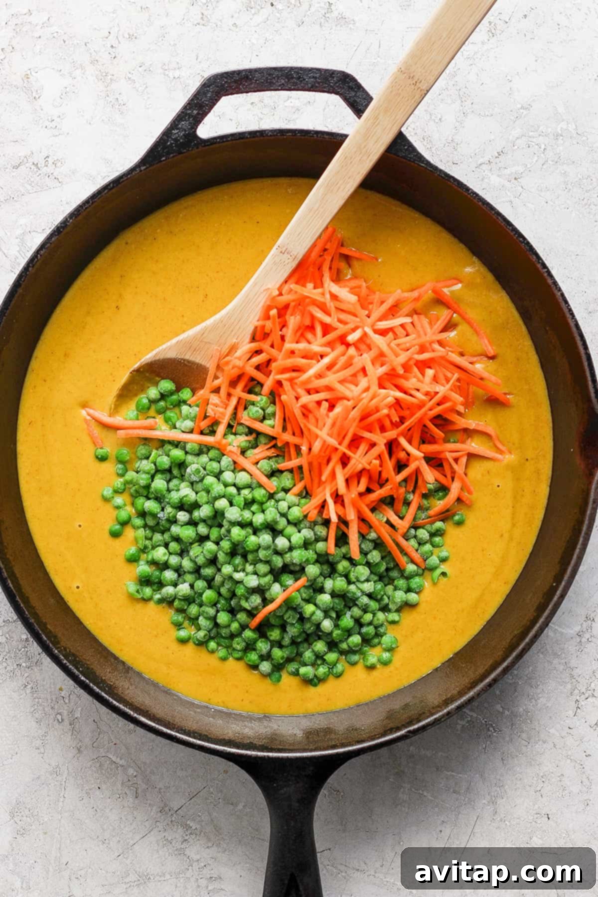 A close-up of a rich and creamy yellow curry simmering in a cast iron skillet, garnished with bright green peas and shredded carrots, offering a preview of its delicious texture.