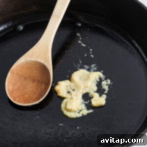 A wooden cooking spoon rests on a black cast iron skillet with remnants of cooked food.