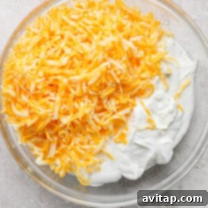A clear glass bowl filled with shredded yellow and white Mexican-style cheese on top of a mound of creamy white whipped cottage cheese, ready to be mixed for the taco lasagna.