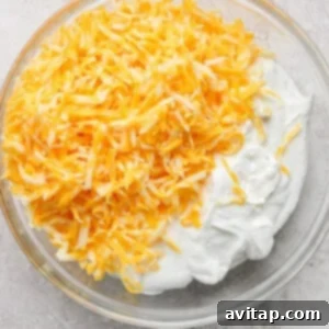 Creamy Cottage Cheese Taco Lasagna 10 A clear glass bowl filled with shredded yellow and white cheese on top of a mound of white, creamy substance on a light-colored surface.