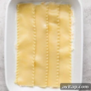 Creamy Cottage Cheese Taco Lasagna 11 A white baking dish containing four uncooked lasagna noodles laid flat on a layer of white sauce.