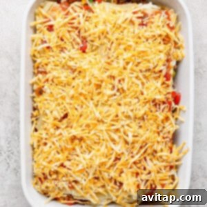 A white baking dish filled with an unbaked Whipped Cottage Cheese Taco Lasagna, generously topped with shredded cheese and ready for the oven.