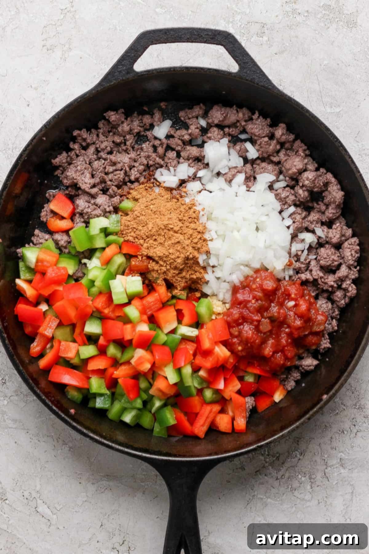 Creamy Cottage Cheese Taco Lasagna 4 A cast iron skillet containing ground beef, diced green and red bell peppers, chopped onions, taco seasoning, and salsa.