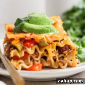 A slice of our high-protein Whipped Cottage Cheese Taco Lasagna, topped with avocado slices and garnished with fresh cilantro, served on a white plate with a fork.