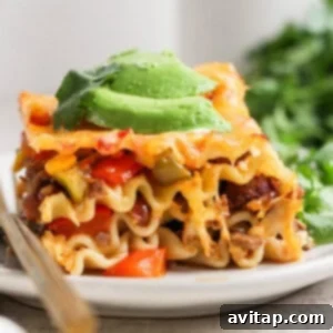 A slice of lasagna topped with avocado slices and garnished with cilantro, served on a white plate with a fork.