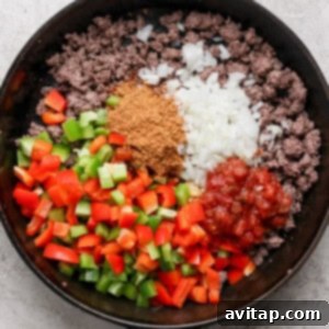 A cast iron skillet containing seasoned ground beef, diced green and red bell peppers, chopped onions, taco seasoning, pinto beans, and salsa, ready for the Whipped Cottage Cheese Taco Lasagna.