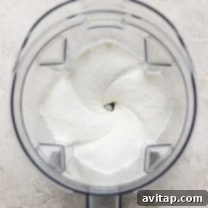 Creamy Cottage Cheese Taco Lasagna 9 Top view of a clear blender jar containing a smooth, creamy white mixture, likely preparing a food or beverage, on a light textured surface.