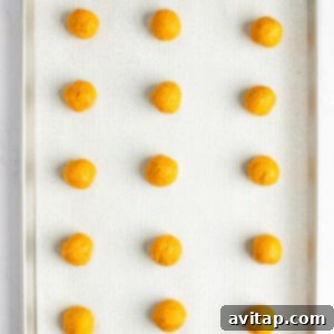 A baking tray with 15 evenly spaced, round, orange dough balls placed on a parchment-lined surface, perfectly portioned and ready for baking.