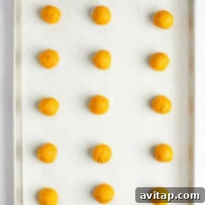 Chocolate Kissed Pumpkin Cookies 10 A baking tray with 15 evenly spaced, round, orange dough balls placed on a parchment-lined surface, ready for the oven.