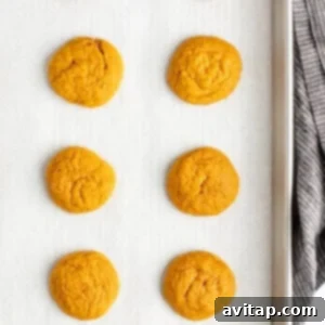 Chocolate Kissed Pumpkin Cookies 11 Eight freshly baked pumpkin cookies resting on a parchment-lined baking sheet, allowing them to cool slightly before moving to a wire rack.