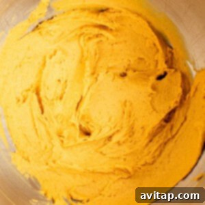 A stainless steel mixing bowl containing smooth, thick orange batter, showcasing the wet ingredients perfectly combined and ready for the dry mixture.