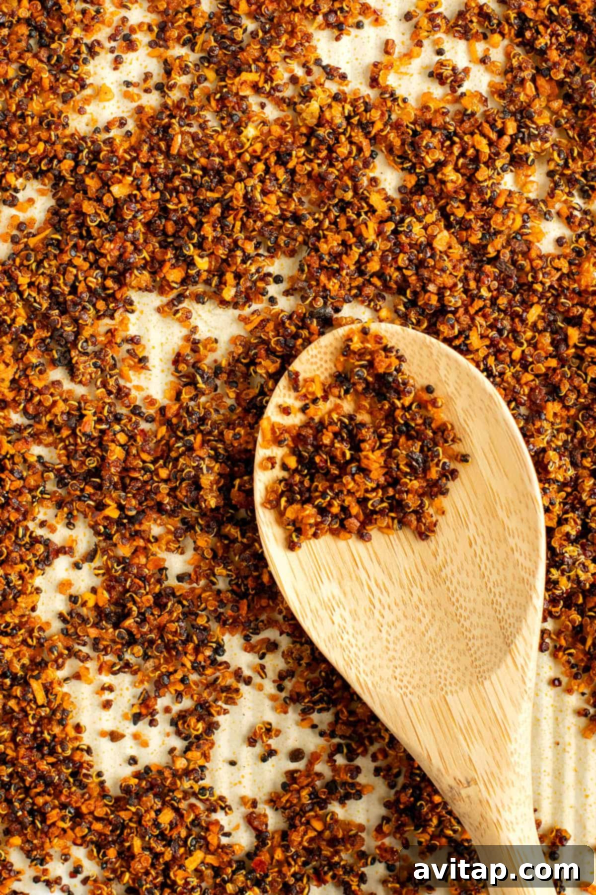 A wooden spoon rests on a surface covered with toasted quinoa grains.