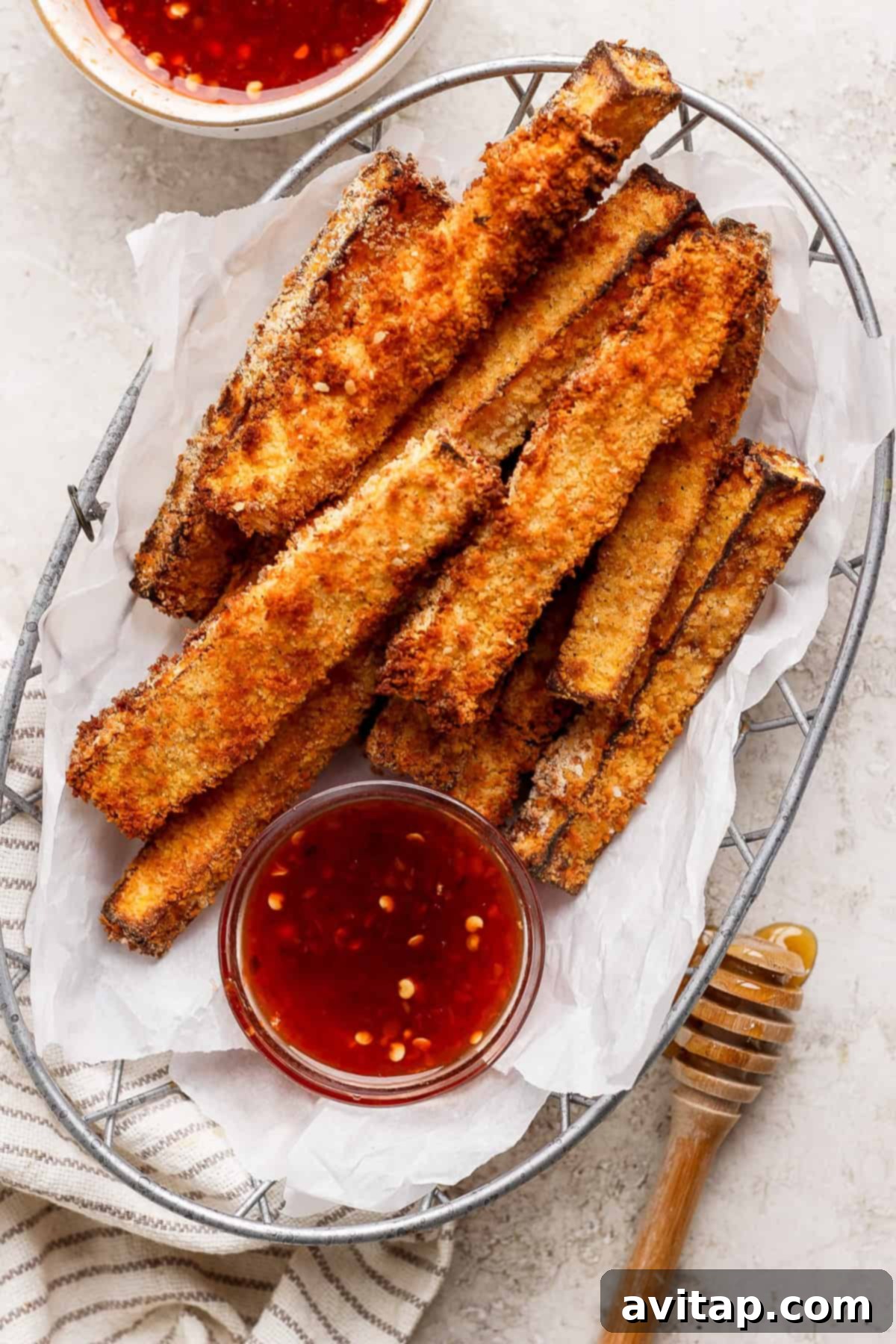 A basket of crispy, breaded butternut squash fries served with two small bowls of red dipping sauce and a a honey dipper.