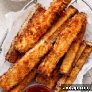 A basket filled with crispy, golden-brown breaded zucchini fries, accompanied by two small bowls of red dipping sauce.