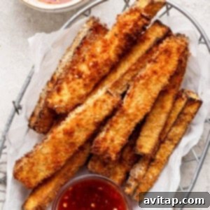 A basket filled with golden brown, crispy breaded vegetable sticks, accompanied by a small bowl of red dipping sauce.
