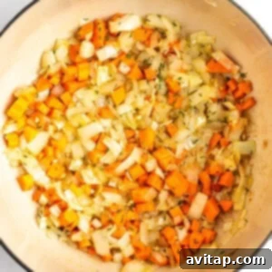 A pot containing sautéed diced onions and carrots.