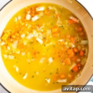 A pot of vegetable soup with chopped onions, carrots, and broth, simmering on the stovetop.