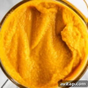 A top view of a glass container filled with smooth, bright orange pumpkin puree on a white marble surface.