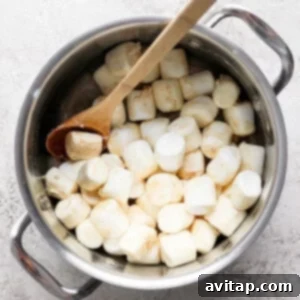 A pot filled with large marshmallows and a wooden spoon placed on a textured surface.