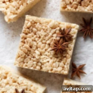 A square rice crispy treat topped with star anise spices, placed on a light-colored surface. Other identical treats and star anise pieces are shown around it.