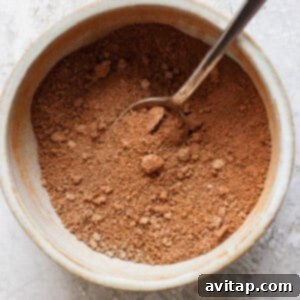 A spoon in a ceramic bowl filled with brown sugar, cinnamon, and softened butter, set on a textured surface, ready to be mixed for the topping.