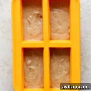 A yellow four-section silicone mold is filled with light brown batter on a light gray textured surface, topped with the cinnamon crunch mixture.