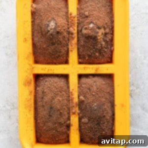 A yellow silicone baking mold with four rectangular cavities, each filled with a brown baked mixture dusted with a light coating of cocoa powder, freshly baked.
