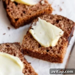 Slices of brown bread topped with thin pats of butter are placed on parchment paper next to a butter knife, ready for serving after cooling.