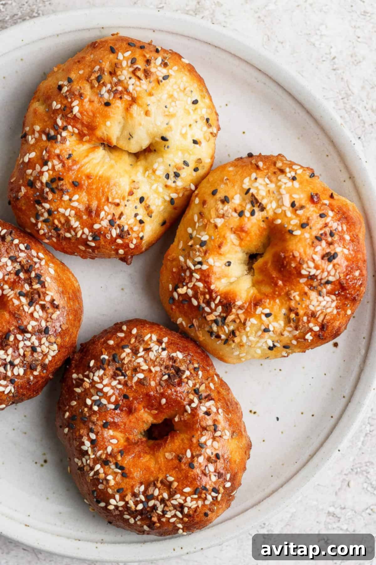 A white plate with four freshly baked bagels topped with sesame seeds and other seasonings, ready to be enjoyed.