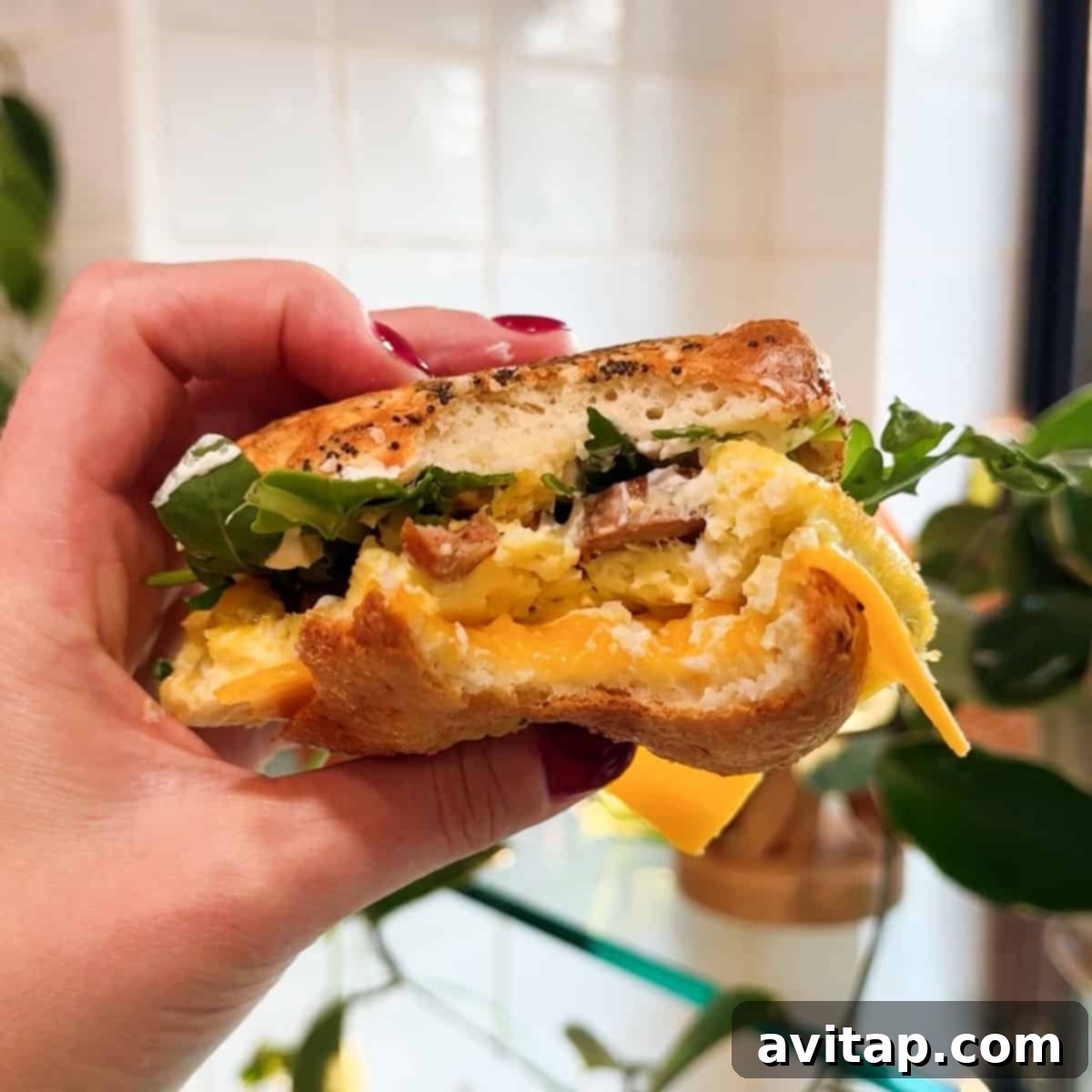 A perfectly assembled breakfast sandwich featuring a sliced bagel, egg, breakfast sausage, cheddar cheese, cream cheese, and fresh arugula, highlighting a delicious serving suggestion.
