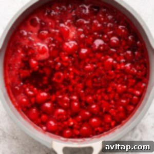 Top view of a pot containing a bubbling red sauce with visible fruit chunks, illustrating the mixture after raspberries have been added and it's cooling.