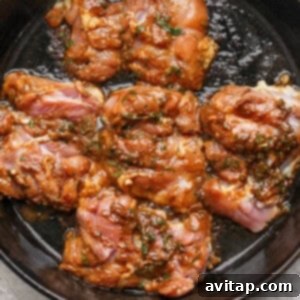 Raw marinated chicken thighs in a dark cast iron skillet, ready to be cooked, showcasing the rich marinade with herbs and a reddish sauce.