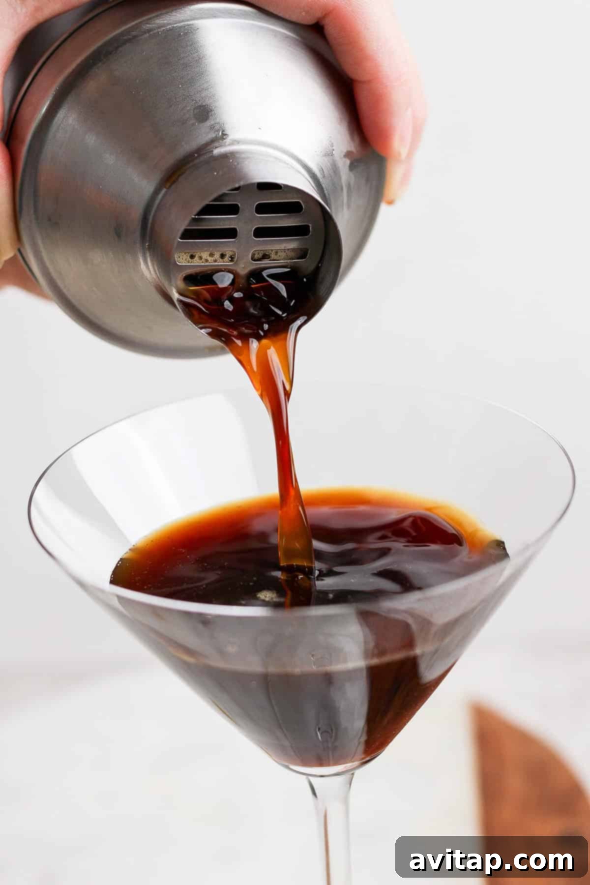 Velvet Brown Sugar Espresso Martini 4 A hand pouring a dark liquid from a metal shaker into a martini glass.