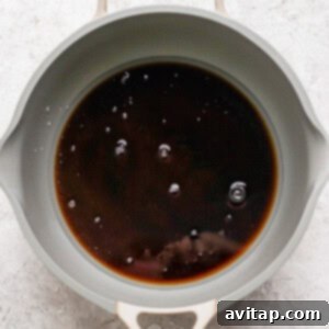 A gray pan containing dark liquid with a few bubbles on the surface, placed on a light gray textured background.