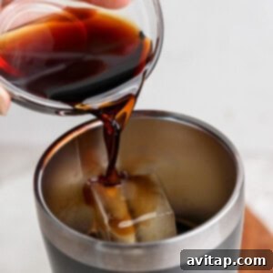 Pouring dark liquid into a stainless steel tumbler with ice.