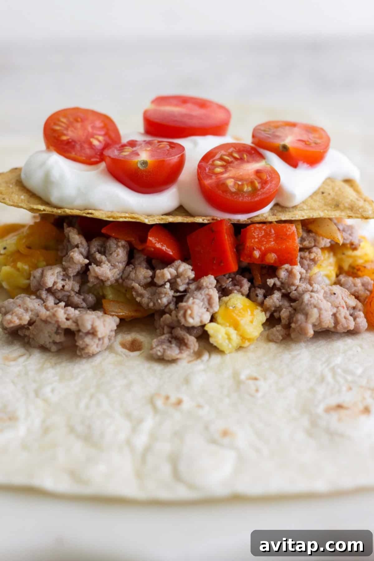 Taco with ground meat, diced red peppers, pineapple, and cherry tomatoes, topped with sour cream.