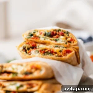 A wrap cut in half, filled with vegetables and cheese, stacked on a parchment paper-lined surface.