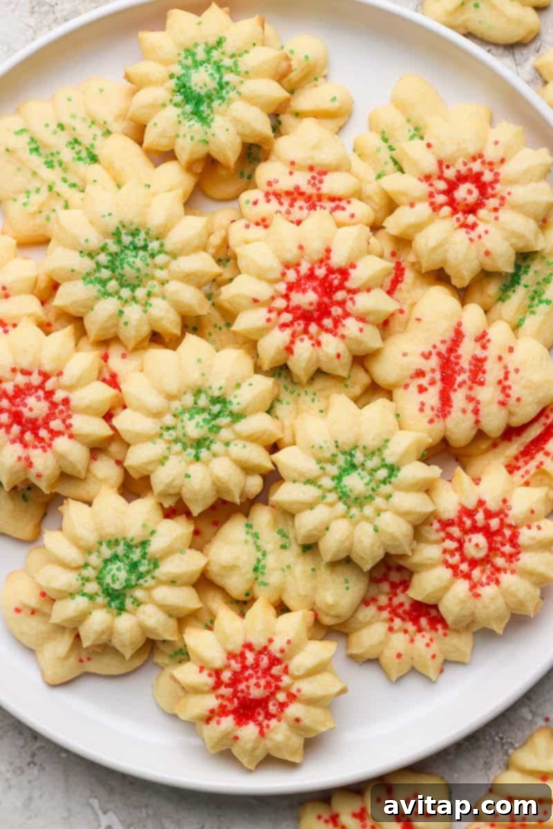 Mabel's Classic Spritz Cookies 2 A white plate filled with flower-shaped cookies topped with festive red and green sprinkles.