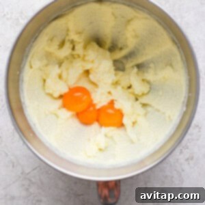 Mixing bowl with creamed butter and sugar, and two egg yolks on top, on a textured surface.