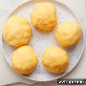 Five yellow dough balls on a speckled plate placed on a light surface.