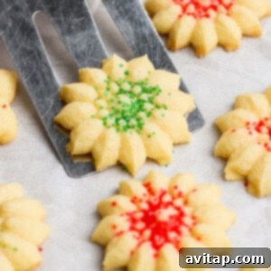 A spatula lifts a star-shaped, green-sprinkled cookie. Other cookies with red sprinkles are on a parchment-lined surface.